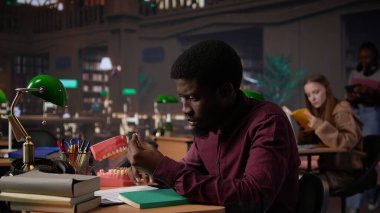 Dişçilik tezi için sahte dişleri inceleyen Afrikalı Amerikalı öğrenci kampüs kütüphanesinde uygun aletlerle stomatoloji araştırması yapıyor. Adam kariyerine hazırlanıyor. Kamera B.