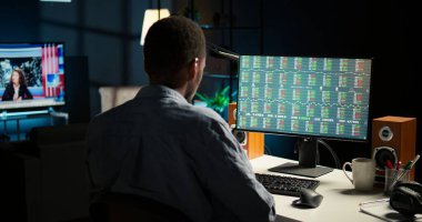 Erkek yatırımcı, şirket kârını artırmak için fonları riske atarak ev bilgisayarındaki canlı eğilimleri takip ediyor. Afro-Amerikalı bir adam piyasa ticaret değerlerine bakıyor, kalkınma planları yapıyor. Kamera A.