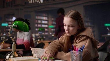 Önemli fikir ve bilgileri ön plana çıkarmaya odaklanan genç öğrenci, üniversite kütüphanesinden veri toplayarak bir edebiyat ödevi üzerinde çalışıyor. Dijital aletler. Kamera B.