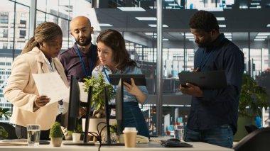 Çok ırklı iş arkadaşları çeşitli ofislerdeki tabletlerin gelir rakamlarına bakıyorlar. Çok ırklı iş arkadaşları beyin fırtınası yapıyor, şirket istatistiklerini karşılaştırıyor, işi bitirmek için çok çalışıyor, kamera A