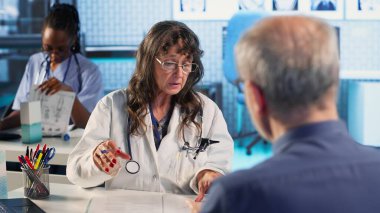 Kıdemli doktor ve hasta modern bir tıp ofisinde teşhis sonuçlarını tartışıyor, gelişmiş teknolojiyi röntgen ve MRI taramalarını gösteren kayıtlar kullanarak sergiliyorlar. Bakım yönetimi. Kamera B.