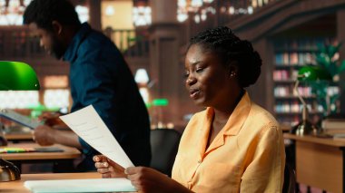 Üniversite kütüphanesi masasında notlar ve kağıtlarla uğraşan bir bayan akademisyen, sınav hazırlıkları için akademik veritabanına danışıyor. Bilgi ve kendini geliştirme. Kamera B.