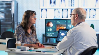 Erkek pratisyen doktor, kanser söz konusu olduğunda önleyici tıp ve risk faktörlerini, MRI taramalarını inceliyor. Doktor ve kadın hasta tedavi seçeneklerini araştırıyor. Kamera B.