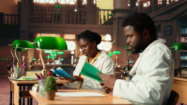 Genç tıp öğrencileri kütüphanede bilgi ve sınıf notlarını karşılaştırıyor, birlikte çalışarak ihtisas yapıyorlar. Öğrenciler ameliyat notlarını okuyarak sağlık yöntemlerini öğreniyorlar. Kamera B.