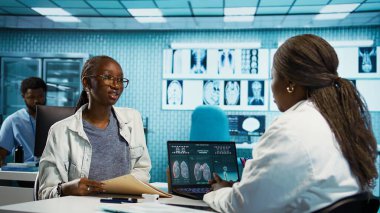 Afro-Amerikalı doktor ve hasta tıbbi kayıtlar hakkında derin bir konuşma yapıyorlar, sonuçları açıklıyorlar ve bir tedavi planı hazırlıyorlar. Sağlık ve iyileşme için ilaç. Kamera B.