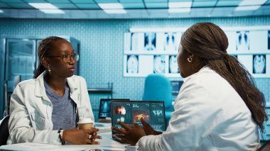 Genç bir hastayla rutin bir kontrol yapan kadın doktor teşhis ve tedavi seçeneklerini radyoloji taramalarıyla analiz ediyor. Profesyonel bir klinikte sağlık hizmeti verileri. Kamera B.