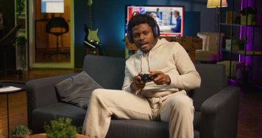 Afrikalı Amerikalı adam evinde yoğun online video oyunları oynuyor, kontrol cihazına spam atak tuşları atıyor. Oyuncu çevrimiçi yarışmaya katılıyor, oyun konsolunda oynuyor. Kamera B.