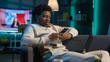 Kendi halinde mutlu bir insan cep telefonuyla eğleniyor. Yanında dizüstü bilgisayarla akıllı telefonuyla arkadaşlarına mesaj atıyor. Konforlu oturma odası vitrinleri ve uzak yaşam tarzında boş vakitler. Kamera A.