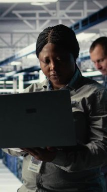 Dikey video veri merkezi teknisyeni altyapı raflarına makine öğrenme yazılımı yerleştirdi. Sunucu çiftliğindeki Afrikalı Amerikalı kadın yapay zeka sistemlerini veri tabanlarıyla eğitiyor.