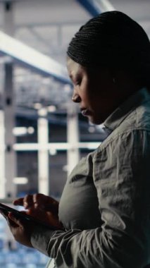 Dikey video bilişim uzmanı endüstriyel platformda yürürken tablet kullanarak sunucu çiftliği aktivitelerini izliyor. Veri Merkezi Sistem Yöneticisi sistemlerin çalıştığından emin olmak için test sonuçlarını gözden geçirir