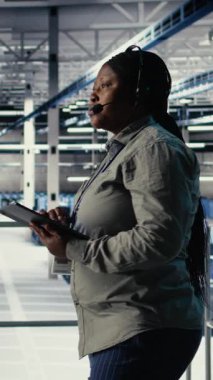 Dikey video sunucu odası teknik destek uzmanı müşterilere güvenli şirket veri yedekleri kurma konusunda rehberlik ediyor. Veri merkezindeki sistem yöneticisi kullanıcıların sunuculardaki sistem hatalarını düzeltmelerine yardımcı olur, kamera A