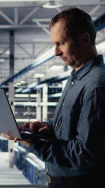 Dikey video teknisyeni tesiste yürürken laptop kullanarak sunucu odası aktivitesini izliyor. Veri Merkezi IT profesyonel incelemeleri sistemlerin doğru çalıştığından emin olmak için test sonuçları