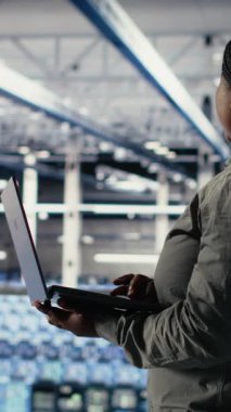 Dikey video Veri Merkezi, en uygun işlevi sağlamak için dizüstü bilgisayar kullanarak yapay zeka yapılandırmalarını araştırır. Sunucu merkezindeki Afrikalı Amerikalı kadın derin öğrenme hataları raporlarını kontrol ediyor