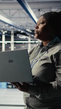 Dikey video veri merkezi yönetimi, işlevsel ölçümleri gözden geçirip, dizüstü bilgisayarla derin öğrenme sürecini izler. Denetim sırasında nöral ağları incelemek için aygıt kullanan Afrikalı Amerikalı kadın