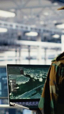 Bilgisayar arayüzü kullanarak veri merkezinde uydu koordinatlarını izleyen dikey video askeri mühendisi. Asker sunucu odasında uydu görüntüleme sistemleri üzerinden keşif verilerini analiz ediyor, kamera B