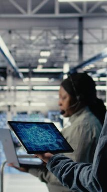 Dikey Veri Merkezi Sistem Yöneticisi, işlevsel ölçümleri gözden geçirip, derin öğrenme süreçlerini izler. Sunucu odası bilişim uzmanı ses kulaklığı takıyor, nöral ağların raporlarını gözden geçiriyor