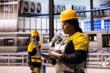 Profesyonel mühendis otomatik fabrikadaki makineleri sistem performansını izlemek için tablet kullanarak inceliyor. Teknisyen akıllı üretim tesisinde robot kolu operasyonları ve endüstriyel otomasyonu garantiliyor.