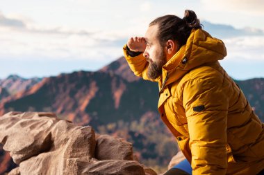 Yürüyüş yolcusu, tepedeki panoramik dağ manzarasına, sonsuz gökyüzüne ve kayalık tepelere hayranlık duymak için ara verir. Zihinsel berraklık için nefes kesici bir zemin oluşturur. Dışarıdaki maceracı..