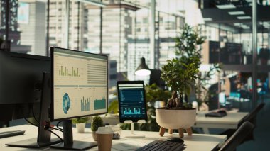 Anahtar performans göstergelerine sahip modern çalışma alanı parlak ofis ortamında saksı bitkileriyle gösteriliyor. Masanın üzerinde bilgisayar ve tablet, ekranda görünen muhasebe rakamlarıyla, görüntüyü kapat