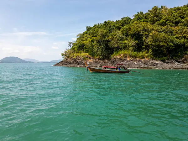 Mavi tropikal bir lagünün içinden hızla geçen ahşap teknenin havadan görünüşü kristal berrak su üzerindeki bir yelkenlinin manzarası. Bereketli sahil kayalıkları ve küçük adalardan oluşan Tayland cenneti.