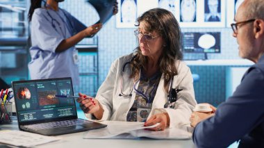 Kadın radyolog, erkek hastayla tümör taramasını inceleyerek, tıbbi teşhis koyuyor ve bağışıklık terapisi, kemoterapi ve daha iyi bir sağlık için yaşam tarzı değişikliklerini tartışıyor. Kamera B.