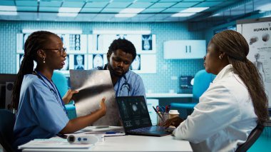 Bu uygulamayı kabinedeki bir doktor uzmandan öğrenen genç hemşirelerden oluşan bir ekip, bir tesiste sağlık yönetimi ve tanı konularını vurguluyor. Afrika kökenli Amerikalı vatandaşlar röntgenleri inceliyor. Kamera B.