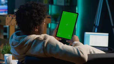 Kendine güvenen teknoloji kullanıcısı oturma odasında izole edilmiş bir maket görüntüsüne bakıyor. Kanepedeki uzaktan kumandalı işi ile rahatlıyor. Afrikalı Amerikalı mutlu yetişkin internette geziniyor. Kamera A.