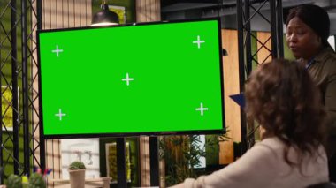 İş kadınlarından oluşan çeşitli grup, finansal planlama ve stratejik güncellemeler için izole edilmiş alan için televizyon ekranını kullanarak profesyonel bir ofiste kroma anahtar monitörü yakınında işbirliği yapmaktadır. Kamera B.