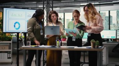 İş kadınları planlama, analiz ve tahminler üzerinde çalışmak üzere belge ve dizüstü bilgisayarların etrafında birleşik bir takım olarak toplanıyorlar. Sonuçlara ve şirket liderliğine odaklanan ortaklar. Kamera A.