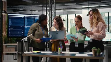 Çeşitli kadın grupları proje geliştirme ve kurumsal feminizm ve stratejik hizalama yoluyla elde edilen başarıyı temsil eden canlı bir modern ofiste göstergeleri tartışıyor. Kamera A.