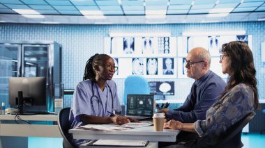 Afrika kökenli Amerikalı hemşire laboratuvar sonuçlarını değerlendiriyor ve yaşlı bir çiftle iyileşme planını tartışıyor. Hastanedeki profesyonel hasta etkileşimi. İnceleme sonuçları ve analizler. Kamera A.