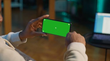 Afrikalı Amerikalı, modern moda evinin rahatlığı için yeşil ekranlı bir cihaz kullanıyor, kanepede oturuyor ve oturma odasında çalışıyor. Kendinden emin mutlu genç adam. Kamera A.