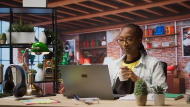 Evdeki ofis masasında çalışan, kahve içen, internette gezinen, bilgi toplayan biri. İş için veri bulmak için arama motorlarını kullanırken sıcak içecekten hoşlanan kadın, kamera A