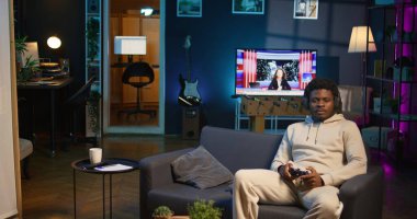 Evinde video oyunu oynayan neşeli bir adam işten izin gününün tadını çıkarıyor. Siyah oyuncu oyun konsolunda online çok oyunculu atıcılarla savaşıyor. Kamera B.