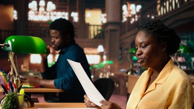 Üniversite kütüphanesi masasında notlar ve kağıtlarla uğraşan bir bayan akademisyen, sınav hazırlıkları için akademik veritabanına danışıyor. Bilgi ve kendini geliştirme. Kamera A.