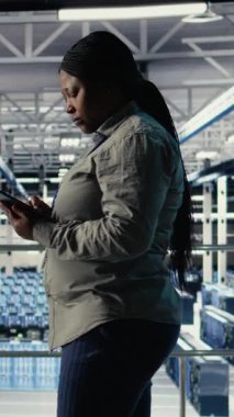 Dikey video bilişim uzmanı endüstriyel platformda yürürken tablet kullanarak sunucu çiftliği aktivitelerini izliyor. Veri Merkezi Sistem Yöneticisi sistemlerin çalıştığından emin olmak için test sonuçlarını gözden geçirir