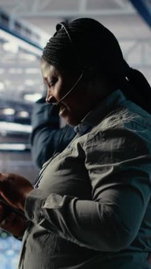 Dikey video sunucusu merkezi teknik destek uzmanı şirket müşterilerine güvenli veri yedekleri kurma konusunda rehberlik ediyor. Veri merkezindeki Afrikalı Amerikalı kadın kullanıcıların sunuculardaki sistem hatalarını düzeltmelerine yardım ediyor