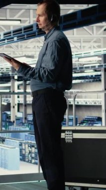 Dikey video sunucu merkezi bilişim uzmanı müşterilere hayati önem taşıyan şirket bilgilerini korumak için güvenli veri yedekleri kurma konusunda rehberlik ediyor. Veri merkezi çalışanı, sunuculardaki sistem hatalarını düzeltmeye yardımcı olur, kamera A