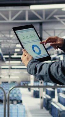 Tablet ekranındaki altyapı grafiklerini kontrol eden veri merkezi çalışanının dikey videosu. Sistem sırasında veri tablolarını incelemek için sunucu odasındaki endüstriyel platformda bilişim uzmanı