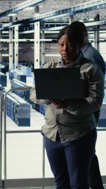 Dikey video veri merkezi yönetimi, teçhizat sistemleri incelemesi sırasında dizüstü bilgisayarla Al 'ın gösterge panelini kontrol ediyor. Sunucu merkezindeki Afrikalı Amerikalı kadın güvenilir olup olmadığını kontrol etmek için yapay zeka araçlarını bilgisayarda test ediyor.