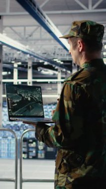 Bilgisayar arayüzü kullanarak veri merkezinde uydu koordinatlarını izleyen dikey video askeri mühendisi. Asker sunucu odasında uydu görüntüleme sistemleri ve kamera A üzerinden keşif verilerini analiz ediyor.