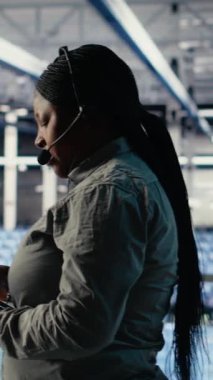 Dikey video sunucu odası teknik destek uzmanı müşterilere güvenli şirket veri yedekleri kurma konusunda rehberlik ediyor. Veri merkezindeki sistem yöneticisi kullanıcıların sunuculardaki sistem hatalarını düzeltmelerine yardımcı olur, kamera B