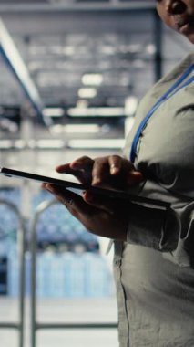 Dikey video Veri Merkezi programcıları yapay zeka panelini tablet kullanarak kontrol eder, sistem gözden geçirir. Sunucu merkezi çalışanları güvenilir performans sağlamak için yapay zeka araçlarını test ediyor, kamera A