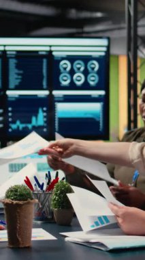 İş kadınlarından oluşan dikey video çeşitliliği ekibi, proje hedefleri belirlemek için şirket ofisindeki masanın etrafında toplanarak strateji raporlarını ve performans verilerini gözden geçiriyorlar. Ortaklık ve güçlenme. Kamera A.