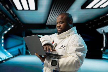 Fütürist uzay aracının içinde uzay giysisi giyen astronot laptop ekranında görev verilerini izliyor. Uzay adamı uzay yolculuğu için ekipman hazırlıyor, not defterinden veri okuyor