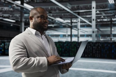 Sunucu çiftliğinde mühendis, güvenlik sistemlerini denetliyor, kurtarma planlarını kontrol ediyor. Veri Merkezi Bilgi İşlem Uzmanı sorun çözme bağlantı sorunları, platformların optimum olarak çalıştığından emin olmak