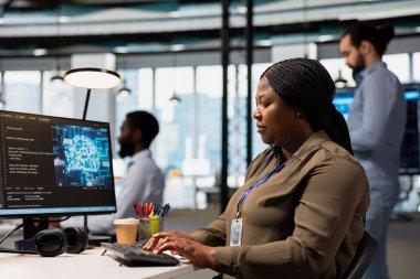 Teknoloji atölyesinde yapay zeka kullanan yazılım mühendisi dijital çözümler üretiyor. Afrika kökenli Amerikalı bilişim uzmanı yapay zeka araçları kullanarak hataları tespit etmek ve düzeltmek için bilgisayar üzerinde çalışıyor.