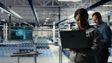 Veri merkezi teknisyeni altyapı raflarına makine öğrenme yazılımı yerleştirdi. Sunucu çiftliğindeki Afrikalı Amerikalı kadın yapay zeka sistemlerini uygulamaları desteklemek için laptop kullanan veri tabanlarıyla eğitiyor.