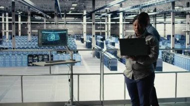 Veri merkezi yönetimi, sondaj sistemleri incelemesi sırasında dizüstü bilgisayarla Al 'ın gösterge panelini kontrol ediyor. Sunucu merkezindeki Afrikalı Amerikalı kadın güvenilir performansı kontrol etmek için yapay zeka araçlarını defterde test ediyor