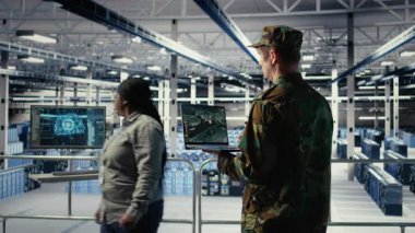 Veri merkezindeki askeri mühendis dizüstü bilgisayar arayüzü kullanarak uydu koordinatlarını takip ediyor. Asker sunucu odasında uydu görüntüleme sistemleri ve kamera A üzerinden keşif verilerini analiz ediyor.